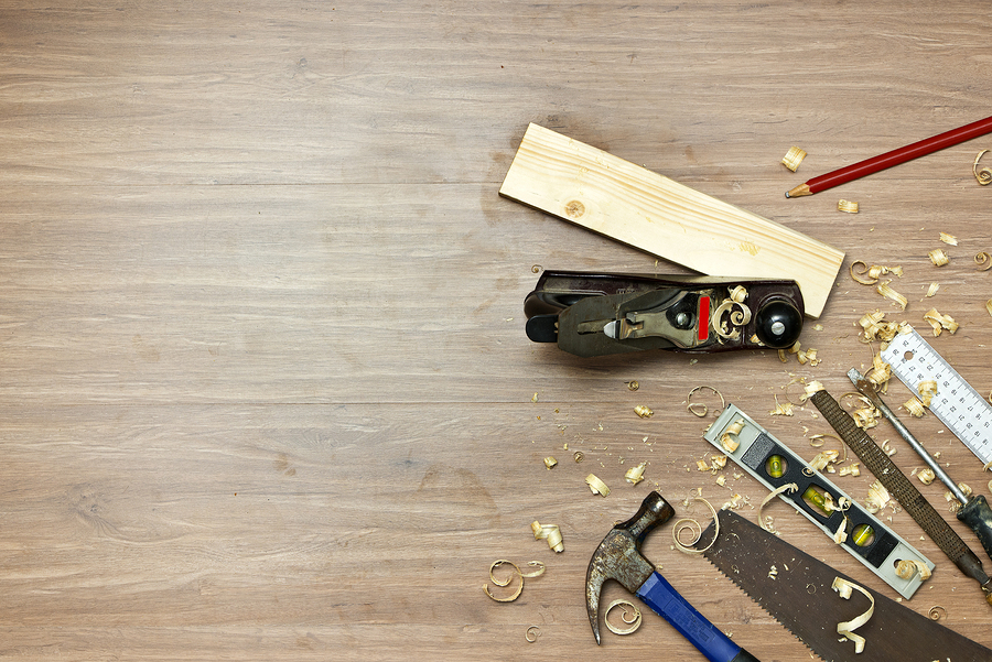 Wood working tools, used in carpentry by a carpenter background. Assorted items, such as a hammer, a wood saw, a spirit level, rasp, screw driver, a carpenter's square and pencil,